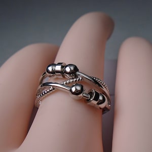 May include: A silver ring with three bands that are intertwined. The bands are decorated with small beads and the ring has a unique design.
