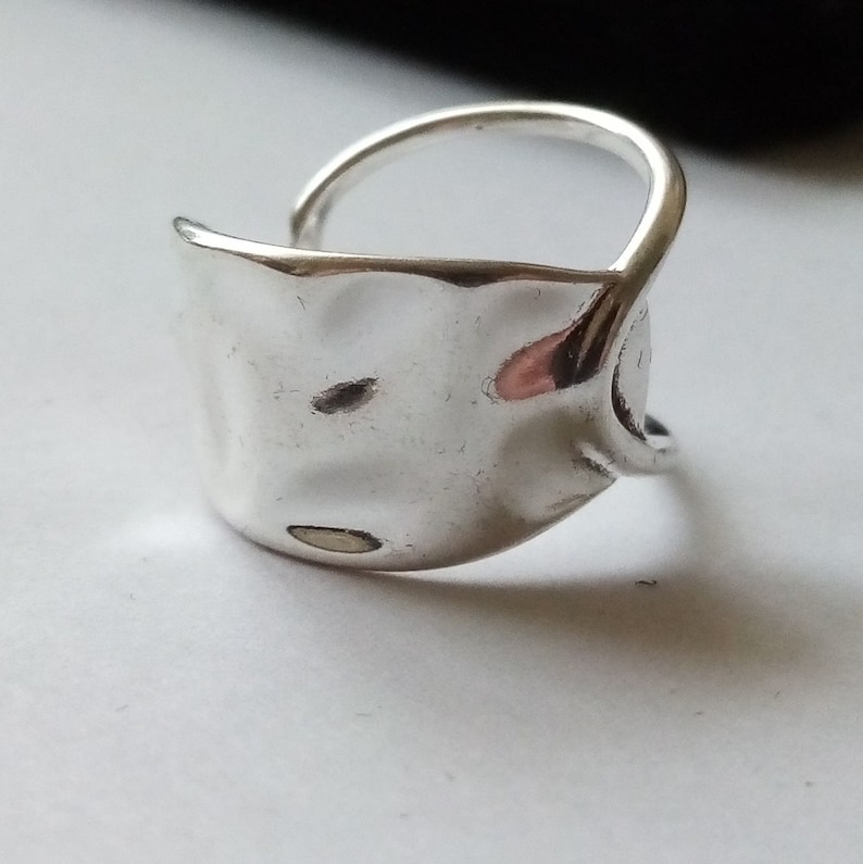 May include: A silver ring with a textured, hammered, oval-shaped band. The band is open on one side and wraps around the finger.