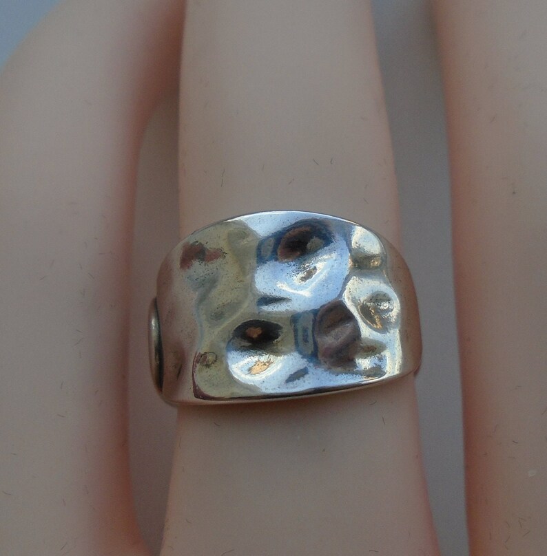 May include: A silver ring with a hammered texture. The ring is wide and has a rounded shape.