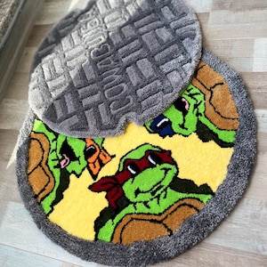 Puede incluir: Una alfombra redonda amarilla con un borde gris presenta cuatro Tortugas Ninja Adolescentes en estilo de dibujos animados. La alfombra está superpuesta sobre una alfombra gris con un diseño de rejilla de alcantarillado.