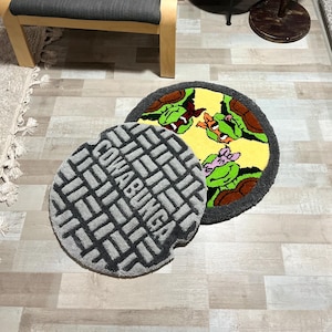 May include: Two round rugs. One is gray with the word "Cowabunga" in large letters. The other rug has a yellow background with green turtle faces and brown and gray borders. The rugs are on a light wood floor.