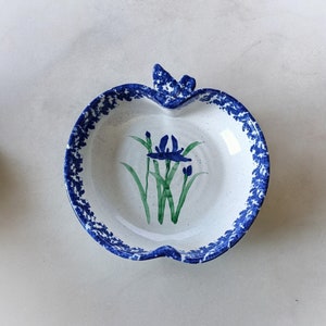 May include: A white ceramic apple-shaped dish with a blue and white floral design. The dish has a scalloped edge and a small handle on top.