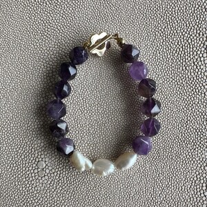 May include: A purple and white gemstone bracelet with a gold clasp. The bracelet is made with faceted amethyst beads and white baroque pearls.