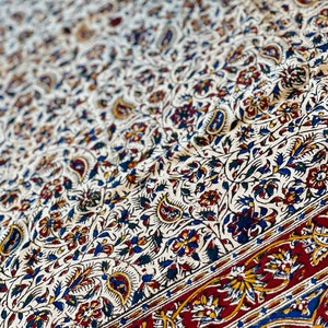 May include: A white tablecloth with a paisley and floral pattern in shades of blue, red, and yellow. The tablecloth has a red border with a paisley design.