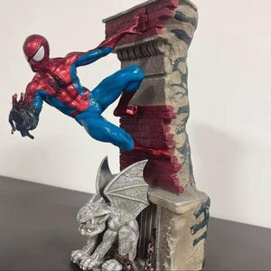 May include: A Spider-Man figurine in a dynamic pose, clad in a red and blue suit, clinging to a brick wall. A gargoyle statue sits below. The statue is detailed with a mix of colors and textures, creating a striking collectible.