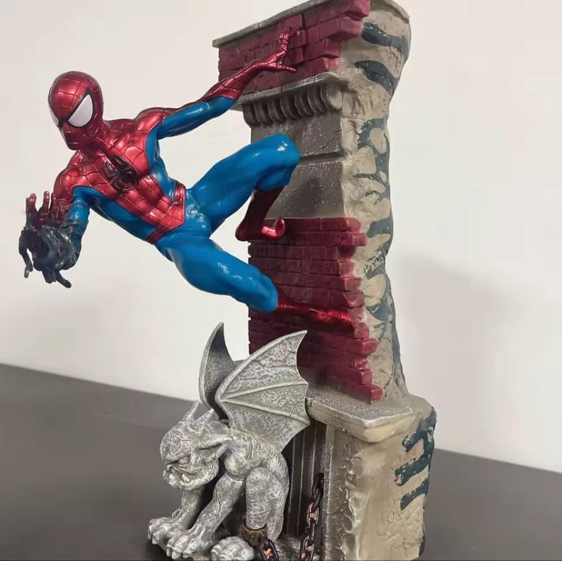 May include: A Spider-Man figurine in a dynamic pose, clad in a red and blue suit, clinging to a brick wall. A gargoyle statue sits below. The statue is detailed with a mix of colors and textures, creating a striking collectible.