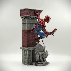 May include: A detailed figurine of Spider-Man in a dynamic pose, clinging to a brick and stone structure. The figure is predominantly red and blue, with intricate detailing. A gargoyle statue is at the base of the structure.