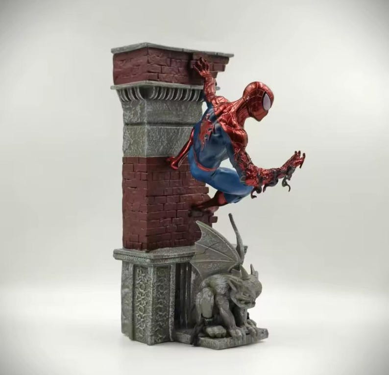 May include: A detailed figurine of Spider-Man in a dynamic pose, clinging to a brick and stone structure. The figure is predominantly red and blue, with intricate detailing. A gargoyle statue is at the base of the structure.