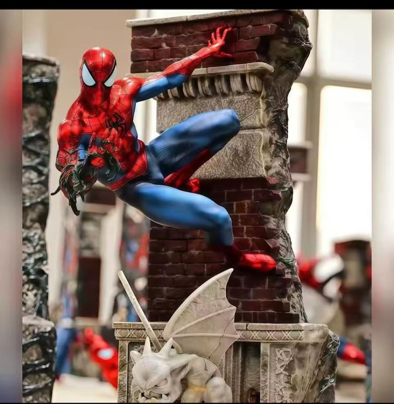 May include: A detailed figurine of Spider-Man in a dynamic pose, clinging to a brick wall. The figure is in a classic red and blue costume, with intricate detailing. The statue is part of a larger display, with other figures visible in the background.