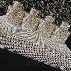 Könnte beinhalten: Fünf klare Glasflaschen, die mit funkelnden Strasssteinen bedeckt sind. Die Flaschen sind in einer Reihe auf einer glitzernden Oberfläche angeordnet.