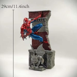 May include: A Spider-Man figurine, approximately 11.4 inches tall, in a dynamic pose climbing a brick wall. The figure is red and blue, with a detailed gargoyle statue at the base. The wall is a mix of red brick and gray stone.