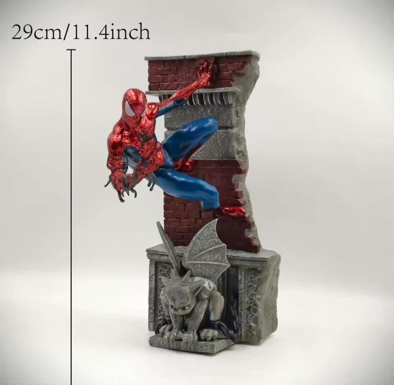 May include: A Spider-Man figurine, approximately 11.4 inches tall, in a dynamic pose climbing a brick wall. The figure is red and blue, with a detailed gargoyle statue at the base. The wall is a mix of red brick and gray stone.