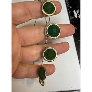 May include: A gold-tone chain necklace featuring five circular pendants with faceted dark green stones. The necklace is displayed next to a black ruler showing measurements in inches, with the largest pendant measuring 0.5 inches in diameter.