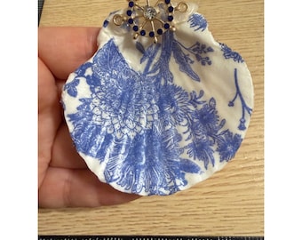 Plato decorativo artesanal de estilo chinoiserie con forma de concha de vieira azul y diseño náutico de timón de barco.