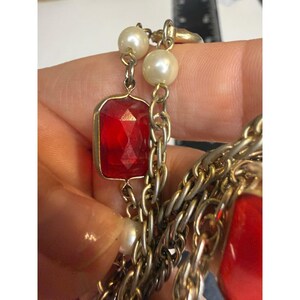 May include: A necklace featuring a silver-toned chain interspersed with white faux pearls and rectangular red faceted glass beads. A black ruler is visible in the background, showing measurements in inches for scale.