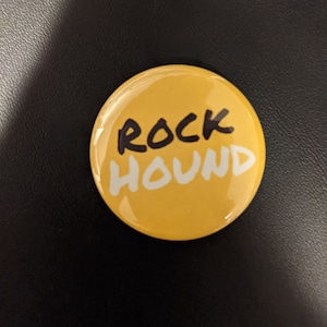 May include: A yellow round button with the words "ROCK HOUND" written in black and white.
