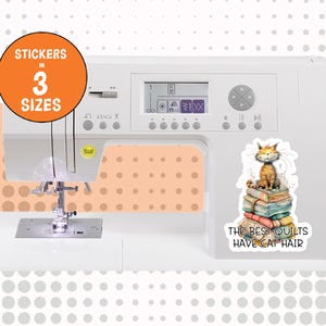May include: A white sewing machine featuring a sticker of an orange tabby cat sitting on a stack of colorful folded quilts. The sticker includes the text "THE BEST QUILTS HAVE CAT HAIR" and an orange circular badge stating "STICKERS IN 3 SIZES".