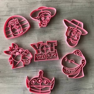 May include: Pink plastic cookie cutters featuring characters from the Toy Story franchise, including Woody, Buzz Lightyear, Rex, and the Toy Story logo.