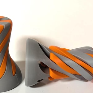 Puede incluir: Dos objetos impresos en 3D con un patrón de espiral. Los objetos están hechos de plástico gris y naranja. El objeto más grande es una forma cilíndrica alta, mientras que el objeto más pequeño es una forma más compleja con una base curva.
