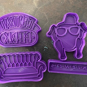 May include: Four purple plastic cookie cutters shaped like the iconic Central Perk logo, a couch, a turkey wearing a hat and glasses, and a rectangle with the text "F.R.I.E.N.D.S."
