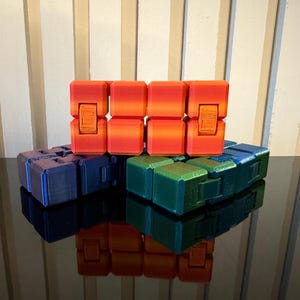 Peut inclure: Trois jouets à manipuler empilés les uns sur les autres. Le jouet du haut est orange et rouge, le jouet du milieu est bleu et le jouet du bas est vert.