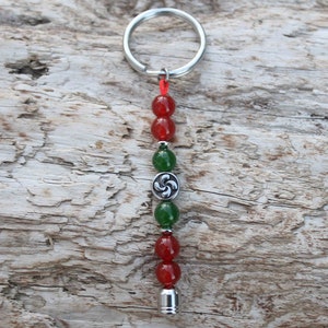 Peut inclure: Un porte-clés argenté avec un pompon de perles rouges et vertes. Le pompon est orné d'un charme argenté avec un motif de nœud celtique.