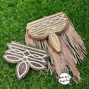 May include: Two decorative fabric embellishments with a geometric design. The embellishments are in shades of brown, gold, and white. The embellishments are on a green grass background. The text "Cute as a Bug's Ear" is visible in the bottom right corner of the image.