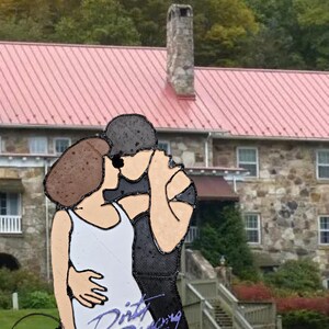 May include: A black and white illustration of a couple dancing, with the words "Dirty Dancing" written in purple below them. The illustration is in front of a stone building with a red roof.