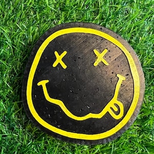 Könnte beinhalten: Ein schwarzer und gelber Smiley-Untersetzer mit gelber Umrandung und zwei gelben X als Augen.