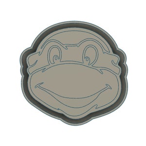 May include: A gray cookie cutter shaped like a Teenage Mutant Ninja Turtle's head. The cutter has a detailed outline of the turtle's face, including eyes, nose, and mouth.