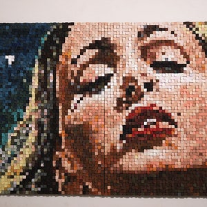 Puede incluir: Un primer plano de un retrato en mosaico de una persona con los ojos cerrados y los labios ligeramente entreabiertos. El mosaico está hecho de pequeños cuadrados de madera de colores.