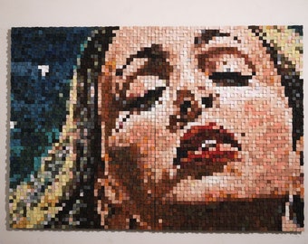 May include: A close-up of a mosaic portrait of a person with their eyes closed and lips slightly parted. The mosaic is made of small, colorful squares of wood.