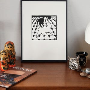K&ouml;nnte beinhalten: Schwarz-wei&szlig;-Druck von zwei Katzen in einem geometrischen Muster. Der Druck ist in einem schwarzen Rahmen gerahmt und h&auml;ngt an einer Wand.