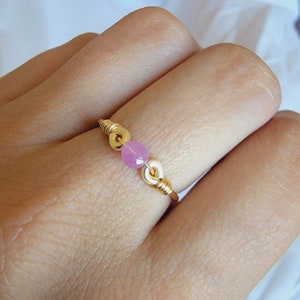 May include: A gold ring featuring a pink gemstone and gold accents.
