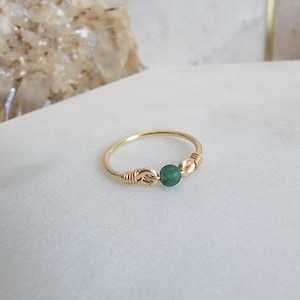 May include: A gold ring featuring a green gemstone and gold wire detailing.
