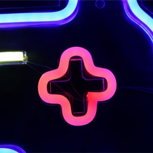 May include: A neon sign shaped like a video game controller with a pink plus button. The sign is lit up in blue and white.