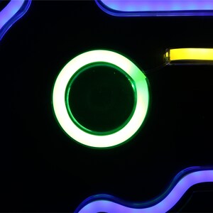 May include: A neon sign with a green circle and a yellow line on a black background. The circle has a smaller green circle inside of it.