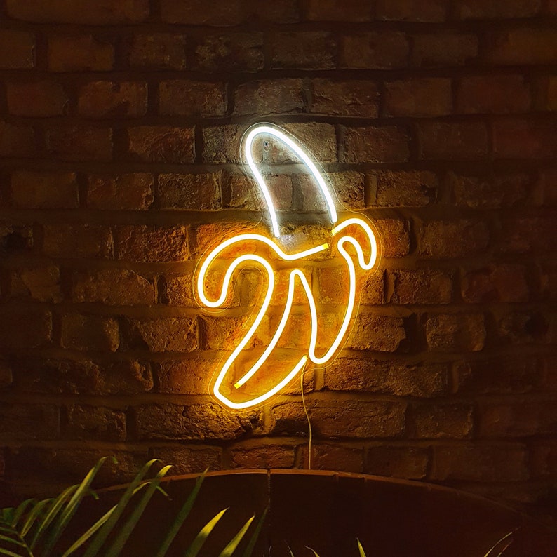 May include: A neon sign shaped like a banana, glowing yellow against a brick wall background.
