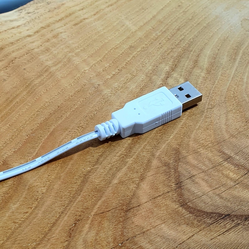 May include: A white USB cable with a standard USB connector. The cable is lying on a wooden surface.