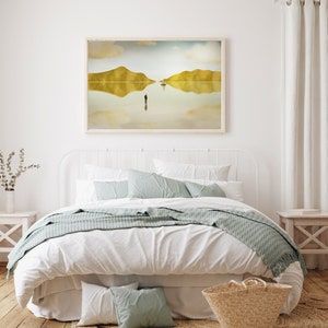 Puede incluir: Una cama blanca con una cabecera blanca y una funda n&oacute;rdica blanca. La cama tiene una manta de tiro azul claro y dos almohadas azul claro. Hay una cesta de mimbre al pie de la cama y una impresi&oacute;n enmarcada de un paisaje con un reflejo del paisaje en el agua sobre una sola figura de pie en el agua.
