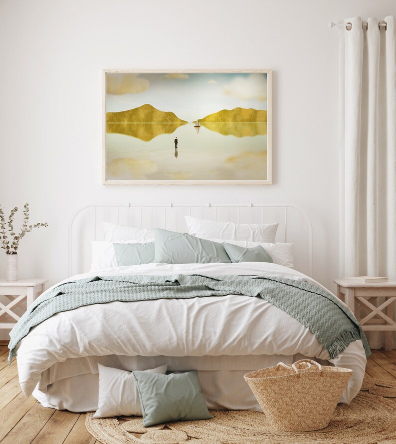 Puede incluir: Una cama blanca con una cabecera blanca y una funda n&oacute;rdica blanca. La cama tiene una manta de tiro azul claro y dos almohadas azul claro. Hay una cesta de mimbre al pie de la cama y una impresi&oacute;n enmarcada de un paisaje con un reflejo del paisaje en el agua sobre una sola figura de pie en el agua.