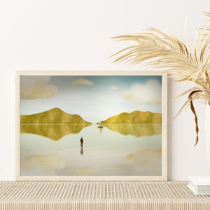 Puede incluir: Una impresi&oacute;n enmarcada de una pintura de paisaje minimalista con un solo velero en un cuerpo de agua tranquilo. La pintura presenta dos colinas verdes reflejadas en el agua, y una figura solitaria de pie en la orilla.