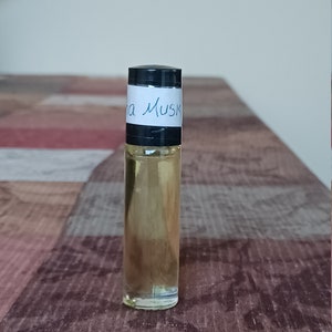 Może przedstawiać: Przezroczysta szklana butelka z rolką z czarną zakrętką i białą etykietą z napisem "Ina Musk".