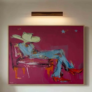 Puede incluir: Pintura abstracta de una persona con sombrero y botas de vaquero, sentada en una silla, sobre un fondo magenta. La figura lleva ropa azul y botas rojas. La pintura cuelga sobre un sofá a rayas y una mesa de centro de madera.