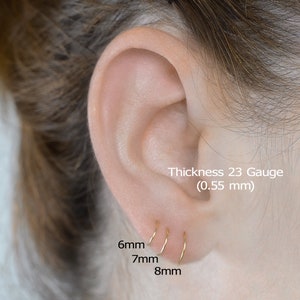 May include: Three gold hoop earrings in different sizes: 6mm, 7mm, and 8mm. The earrings are shown in a person's ear. The text 'Thickness 23 Gauge (0.55 mm)' is also visible.