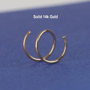 May include: A pair of intertwined gold-colored earrings against a blue background. The earrings are in a spiral shape, with the text "Solid 14k Gold" above them. The earrings are made of solid 14k gold.