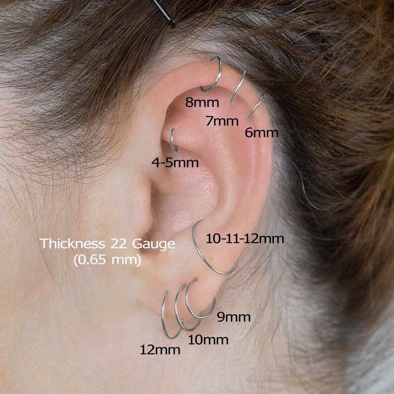 May include: A close-up of a person's ear with multiple silver hoop earrings in various sizes. The earrings are labeled with their measurements in millimeters: 8mm, 7mm, 6mm, 4-5mm, 10-11-12mm, 9mm, 10mm, and 12mm. The text 'Thickness 22 Gauge (0.65 mm)' is also visible.