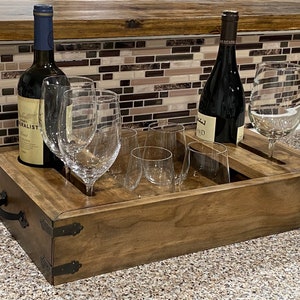 May include: A wooden wine serving tray with two wine bottles and several wine glasses. The tray is rectangular with metal corner accents and handles. The bottles are dark, and the glasses are clear.