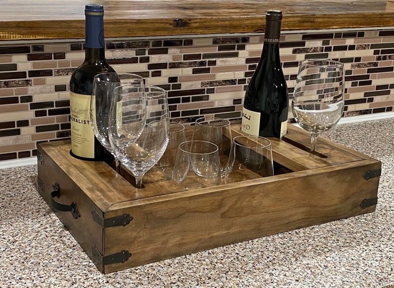 May include: A wooden wine serving tray with two wine bottles and several wine glasses. The tray is rectangular with metal corner accents and handles. The bottles are dark, and the glasses are clear.