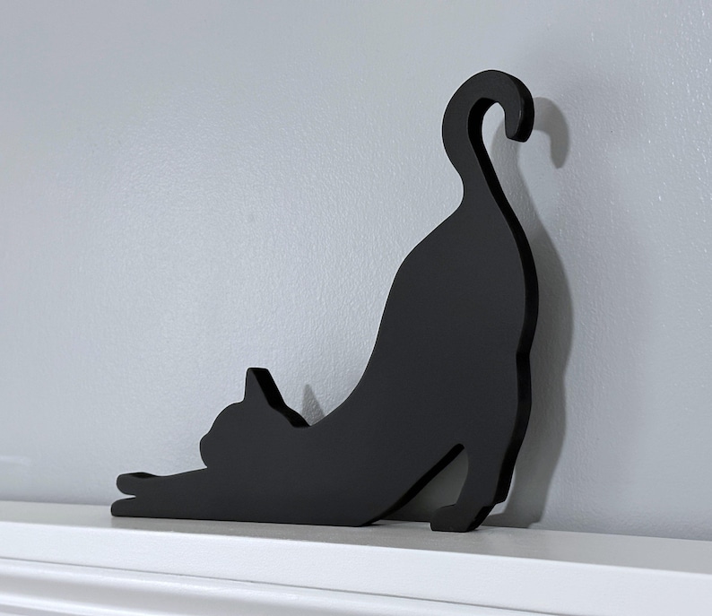 A black wooden cat silhouette wall decor. The cat is in a stretched out pose with its tail curled up. The cat is facing to the left.